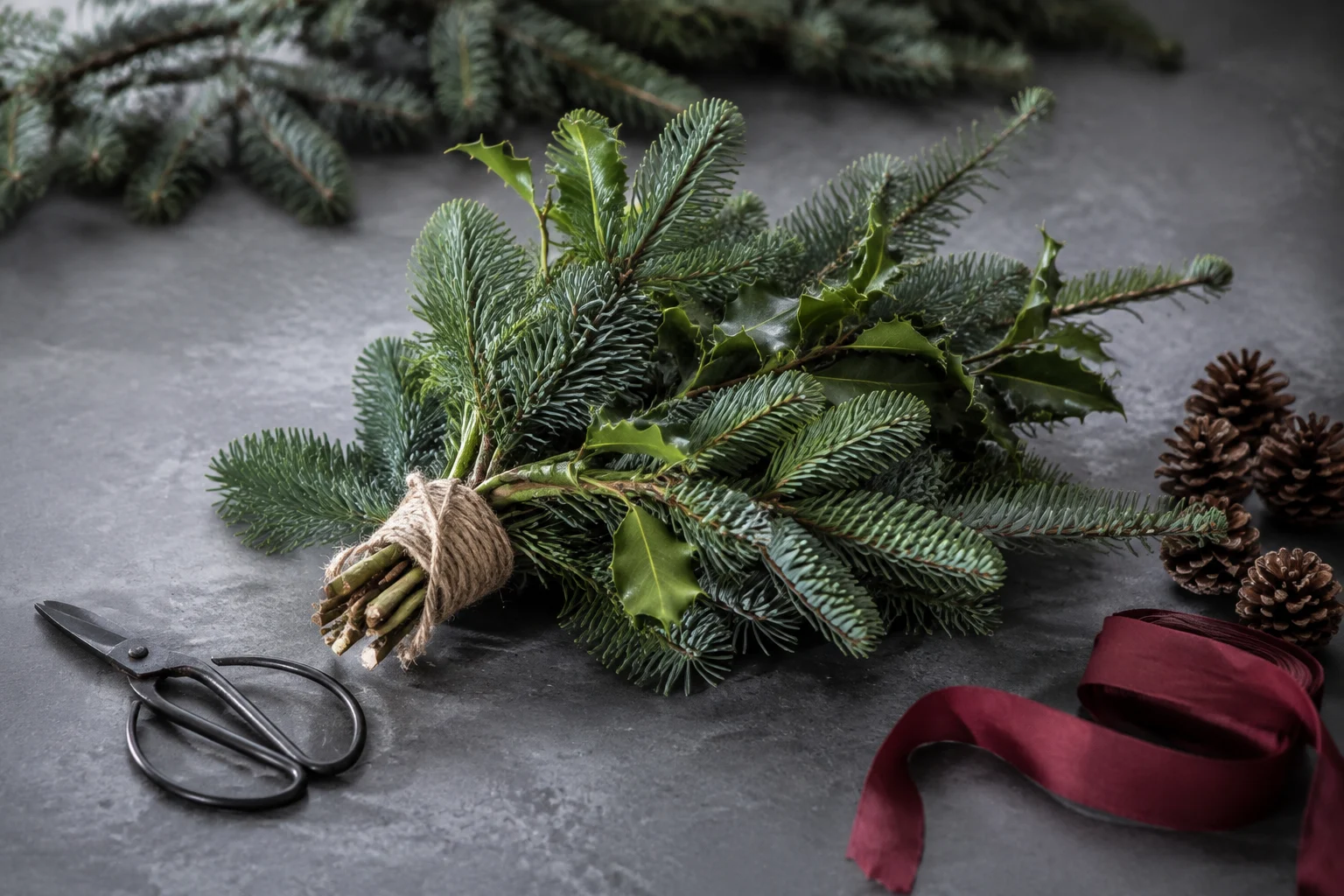 Fresh fir and holly gathered with pine cones and ribbon on a florist’s bench
